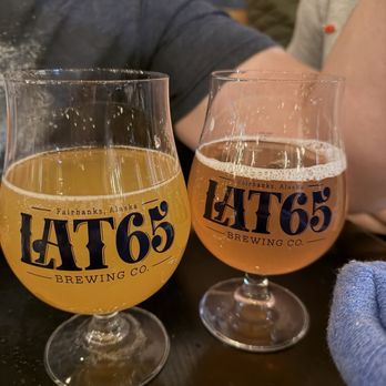 Two Lat 65 Brewing Co. tulip glasses, one hazy golden beer and one amber beer, on a taproom table